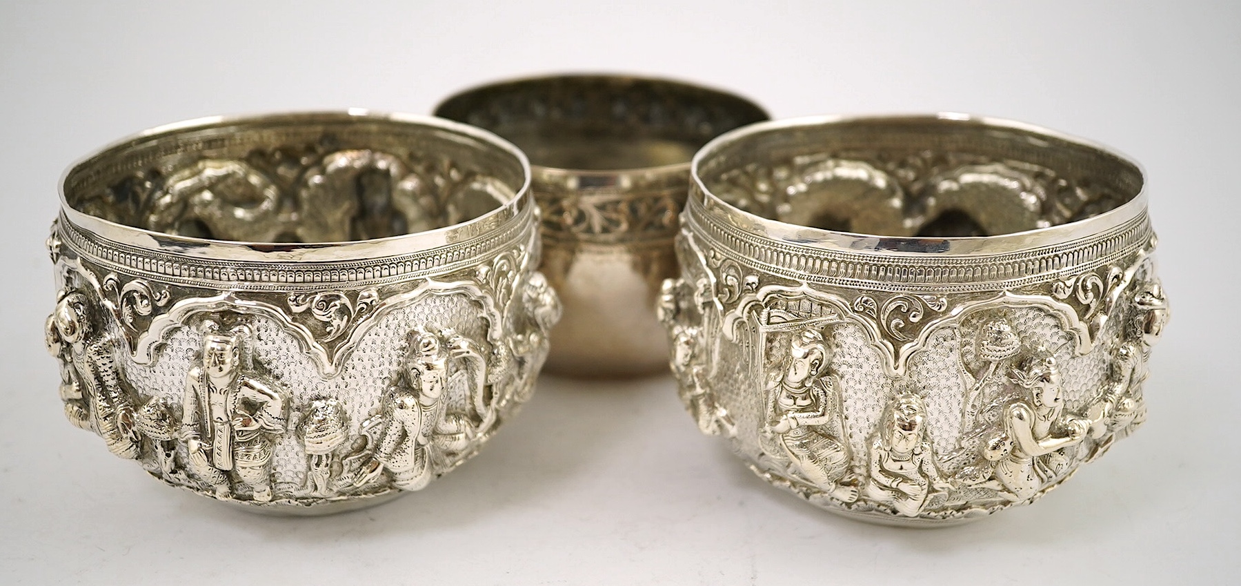 A pair of Burmese white metal bowls, embossed with figures, 12cm diameter, 220 and 224g and a plainer bowl, 110g. Condition – fair